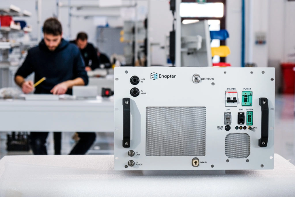 Wasserstoff-Start-up macht sich bereit für Serienproduktion Wasserstoff und im speziellen grüner Wasserstoff wird von vielen Unternehmen als die nächste große Innovation im Energiesektor gesehen. Wasserstoff wird durch Elektrolyse hergestellt, bei der Wasser unter Einsatz von Strom in Wasserstoff und Sauerstoff getrennt wird. Bei grünem Wasserstoff wird dieser mit erneuerbaren Energien erzeugt und ist dadurch CO2-neutral. Viele Unternehmen wollen Anlagen für die Erzeugung von Wasserstoff entwickeln und bauen. Primär steht im Fokus, die Serienreife für die Massenproduktion und damit ein wichtiger Standfuß im zukünftigen Wettbewerb in diesem neuen Markt. Mit dabei sind große Konzerne wie Air Liquide, Linde oder Siemens Energy. Das Start-up Enapter ist den Konzerne dabei schon einen wichtigen Schritt voraus. Gründer Sebastian-Justus Schmidt will die erste Serienproduktion für die eigenen Elektrolyseure aufbauen. „Wir wollen mit unserer Fabrik in Nordrhein-Westfalen den Schritt in die Industrialisierung gehen. Wir kommen mit unseren jetzigen Kapazitäten einfach nicht mehr aus“, sagte Schmidt dem Handelsblatt. Die Idee des Start-up ist dabei vergleichbar mit heutigen Serverfarmen. Das Unternehmen entwickelt kleine Elektrolyseeinheiten, die beliebig erweitert werden können. Wie bei Serverfarmen können die Elektrolyse-Systeme für den jeweiligen Einsatzzweck erweitert und modular zusammengesetzt werden. Dadurch sollen die Kosten deutlich sinken.