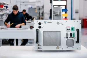 Wasserstoff und im speziellen grüner Wasserstoff wird von vielen Unternehmen als die nächste große Innovation im Energiesektor gesehen. Wasserstoff wird durch Elektrolyse hergestellt, bei der Wasser unter Einsatz von Strom in Wasserstoff und Sauerstoff getrennt wird. Bei grünem Wasserstoff wird dieser mit erneuerbaren Energien erzeugt und ist dadurch CO2-neutral. Viele Unternehmen wollen Anlagen für die Erzeugung von Wasserstoff entwickeln und bauen. Primär steht im Fokus, die Serienreife für die Massenproduktion und damit ein wichtiger Standfuß im zukünftigen Wettbewerb in diesem neuen Markt. Mit dabei sind große Konzerne wie Air Liquide, Linde oder Siemens Energy. Das Start-up Enapter ist den Konzerne dabei schon einen wichtigen Schritt voraus. Gründer Sebastian-Justus Schmidt will die erste Serienproduktion für die eigenen Elektrolyseure aufbauen. „Wir wollen mit unserer Fabrik in Nordrhein-Westfalen den Schritt in die Industrialisierung gehen. Wir kommen mit unseren jetzigen Kapazitäten einfach nicht mehr aus“, sagte Schmidt dem Handelsblatt. Die Idee des Start-up ist dabei vergleichbar mit heutigen Serverfarmen. Das Unternehmen entwickelt kleine Elektrolyseeinheiten, die beliebig erweitert werden können. Wie bei Serverfarmen können die Elektrolyse-Systeme für den jeweiligen Einsatzzweck erweitert und modular zusammengesetzt werden. Dadurch sollen die Kosten deutlich sinken.